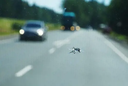 A crack on the windshield from a stone that flew in from under the wheels of a car against the background of the road and oncoming cars