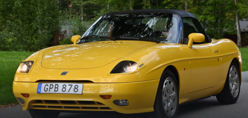 A yellow convertible car cruising down a scenic road under a clear blue sky.